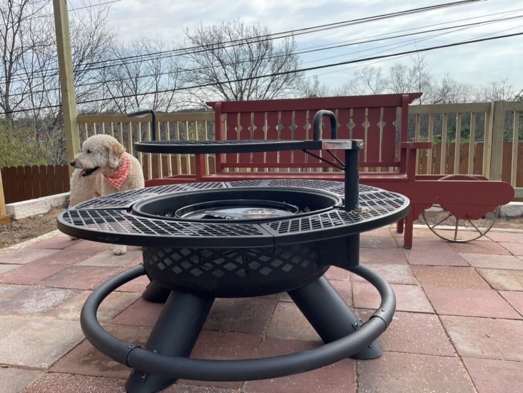 A circular outdoor grill with a metal grate, surrounded by a black metal frame.