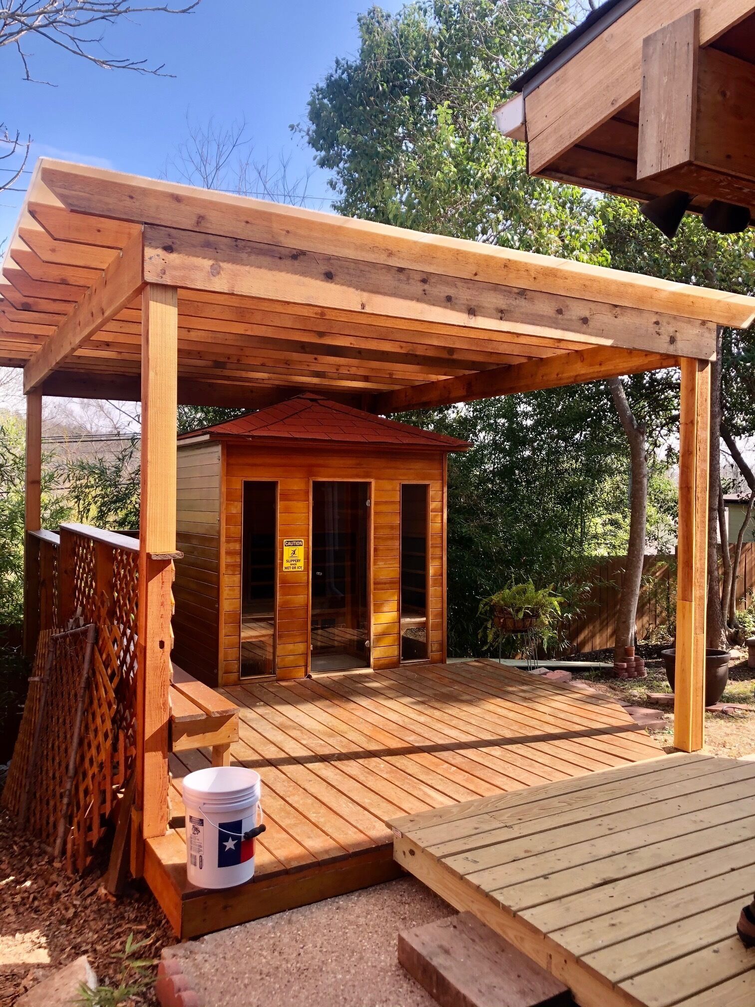 A wooden deck with a covered area, a small building with a caution sign, and a bucket of paint.