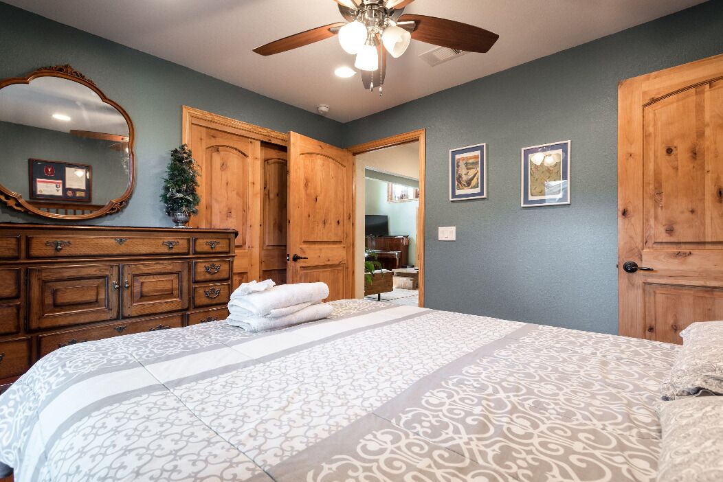A bedroom with a large bed, wooden wardrobe, and a ceiling fan.