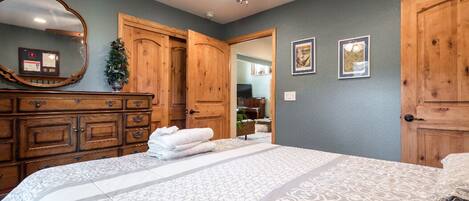 A bedroom with a large bed, wooden wardrobe, and a ceiling fan.