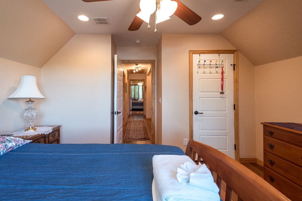 A bedroom with a bed, a nightstand with a lamp, a wooden dresser, and a door with a coat rack.