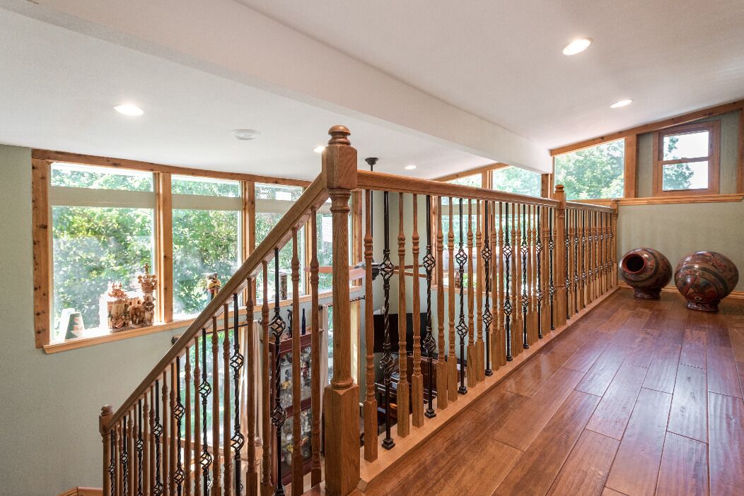A wooden staircase with a railing, large windows, and a view of greenery outside.