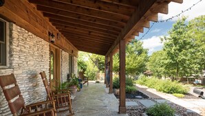 Eine überdachte Veranda mit Steinmauern, Holzstühlen und einem Gartenbereich mit Pflanzen und einem Weg.