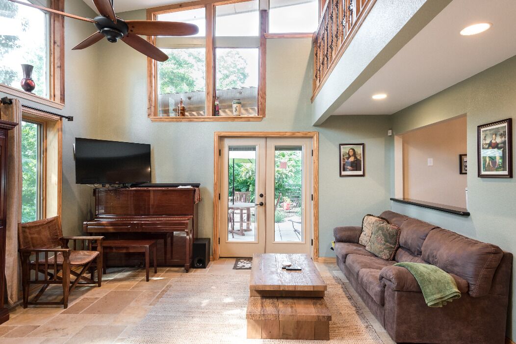 A spacious living room with a piano, a television, a brown leather couch, and a ceiling fan.