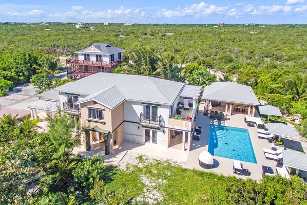 A large house with a swimming pool, multiple balconies, and a lush surrounding landscape.