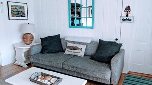 Een woonkamer met een grijze bank, een witte salontafel, een raam met teal kader, een lamp en een klein plankje met een automodel.
