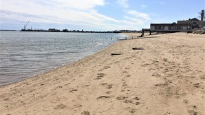 Een zandstrand met voetafdrukken, een steiger en gebouwen op de achtergrond.