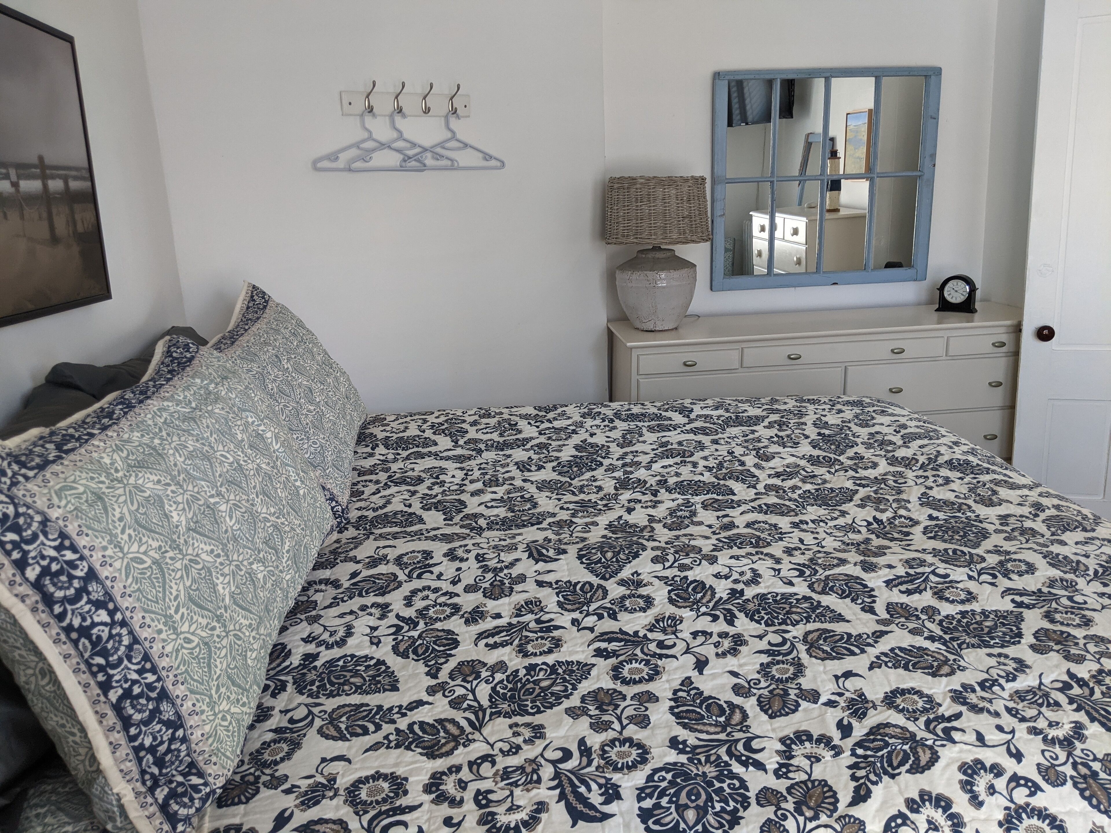A bedroom with a bed, a dresser, a mirror, and a wall-mounted coat rack.