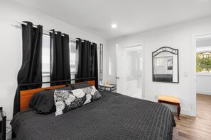 A bedroom with a bed, black curtains, a wooden headboard, a bench, a mirror, and a door leading to a bathroom. - UNIT # 7 Ocean and Downtown view LAUDERDALE BY THE SEA 200+- steps to beach fun (Lauderdale-by-the-Sea)