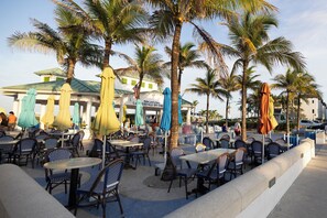 Outdoor seating with umbrellas, palm trees, and a building with a green roof. - UNIT # 7 Ocean and Downtown view LAUDERDALE BY THE SEA 200+- steps to beach fun (Lauderdale-by-the-Sea)