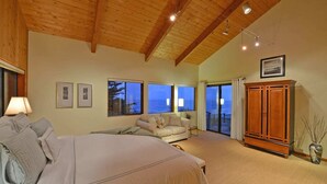 Ein Schlafzimmer mit einem großen Bett, einer Couch, einem Holzschrank und Meerblick durch die Fenster.