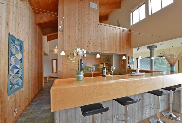 A modern kitchen with wooden cabinetry, a bar area with stools, and pendant lighting.