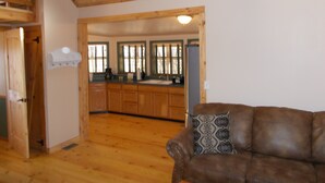 A wooden interior with a brown leather sofa, wooden cabinets, and a kitchen area visible through an open doorway.