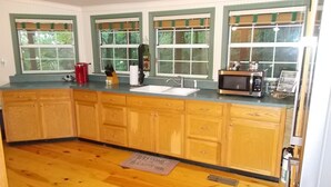 A kitchen with wooden cabinets, a sink, a microwave, and a window with a view of greenery.
