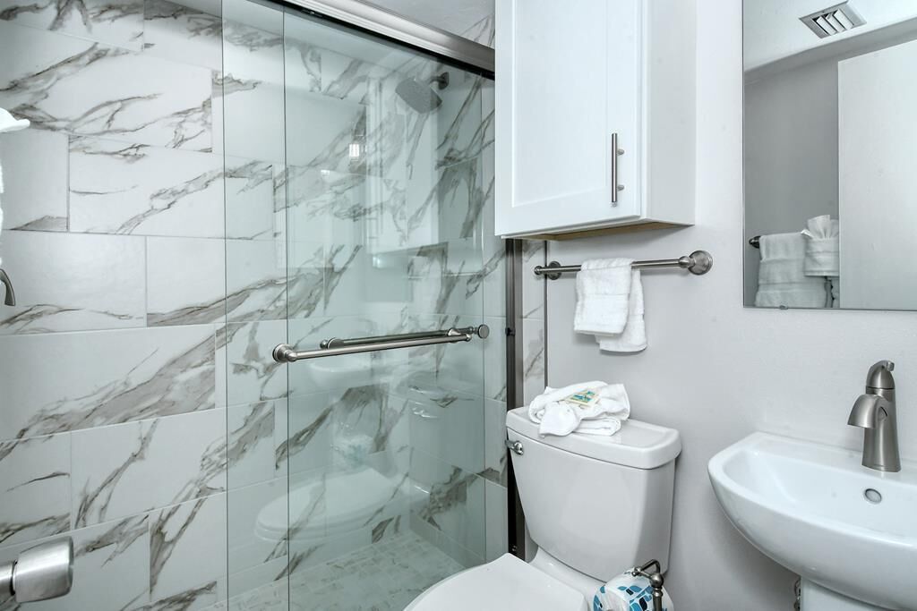 A bathroom with a glass shower enclosure, a white toilet, a sink, and a towel rack.