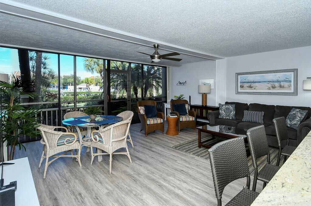 A spacious living area with a large window, a ceiling fan, wicker furniture, and a view of the outdoors.