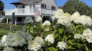 A two-story house with a balcony, a flag, and white hydrangea flowers in the foreground. - Maine Dream Cottage (Biddeford)
