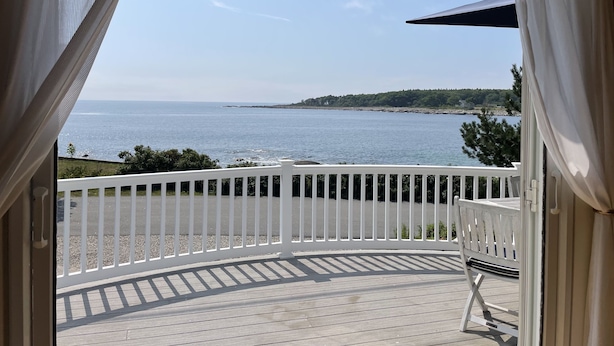 A view from a balcony with a wooden deck, white railing, and a bench. - Maine Dream Cottage (Biddeford)