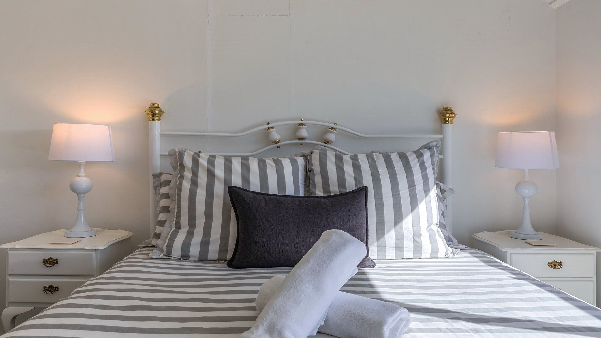 A neatly made bed with striped bedding, two bedside lamps, and a headboard with decorative elements.