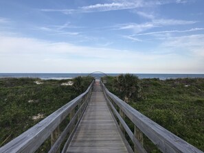 A wooden boardwalk leading to a beach with a clear sky.