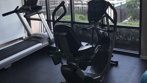 Un gimnasio con cinta de correr, elíptica y máquina de remo. Amplias ventanas ofrecen vistas a zonas verdes exteriores.