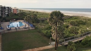Zona de piscina con sillas de descanso, una palmera y vista a la playa.