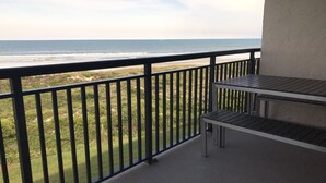 Un balcón con vista al océano, una mesa de metal y sillas.