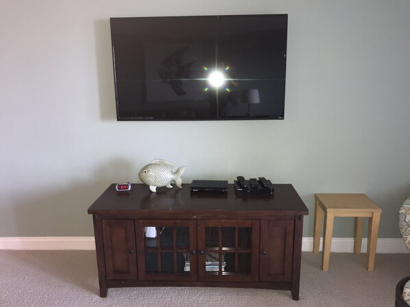 A television mounted on a wall, a wooden cabinet with glass doors, and a small wooden stool.