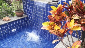 A small outdoor hot tub with a waterfall feature, surrounded by potted plants and a tiled pool area. - Tranquility on the right side of Ferradura (Buzios)