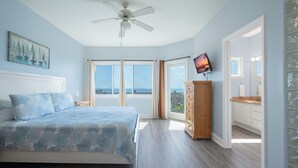 Een slaapkamer met een bed, een nachtkastje, een houten dressoir, een plafondventilator en een televisie aan de muur.