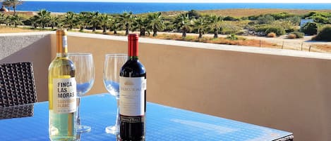 A table with two wine bottles and two glasses on a balcony overlooking a coastal landscape.