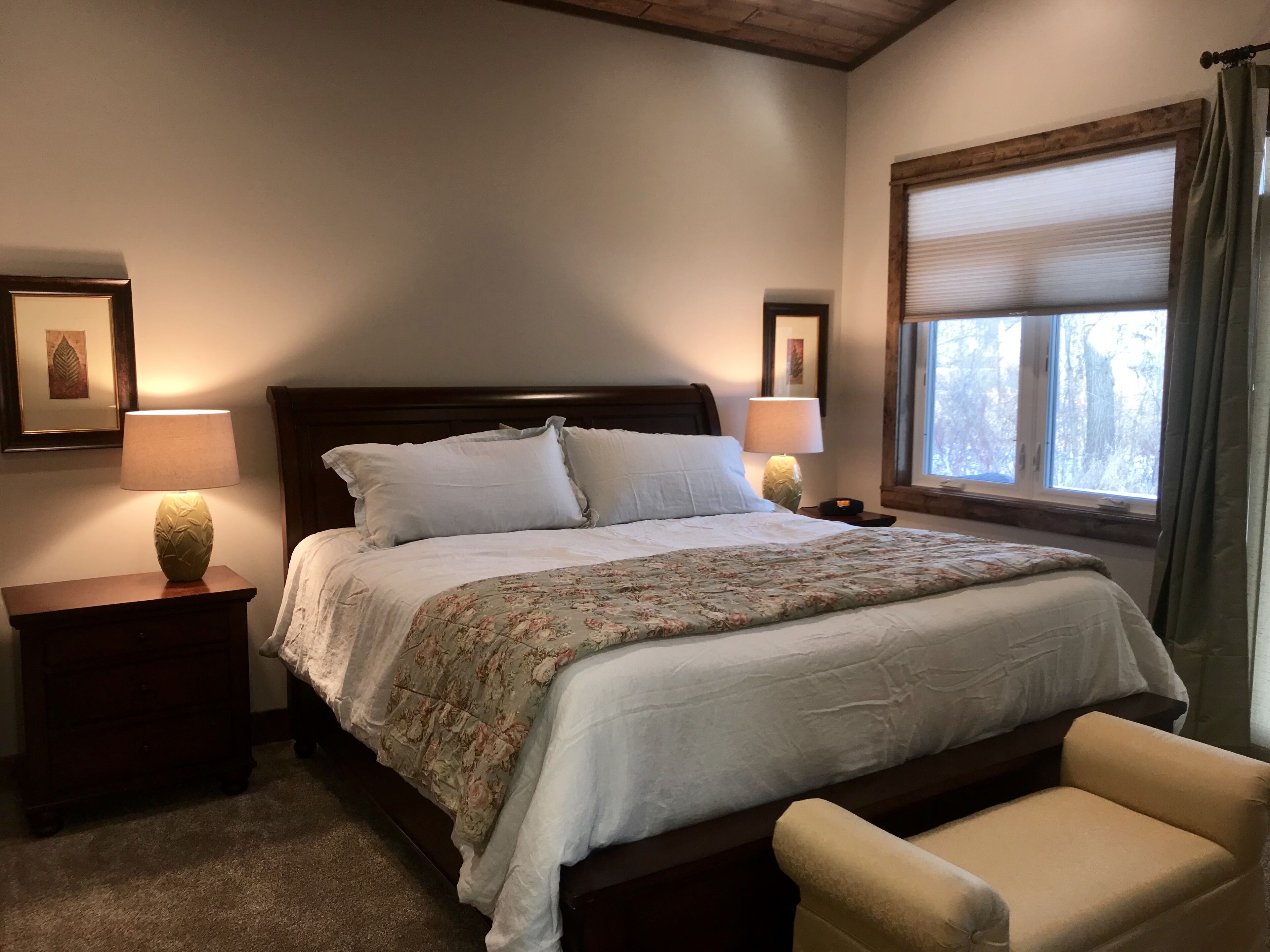 Een slaapkamer met een groot bed, twee nachtkastjes, een stoel en een raam met gordijnen.