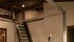 Ein Schlafzimmer mit einer Holztreppe, einem Bett mit einem gemusterten Duvet, einer hölzernen Kommode und einer kleinen Vase mit Blumen.