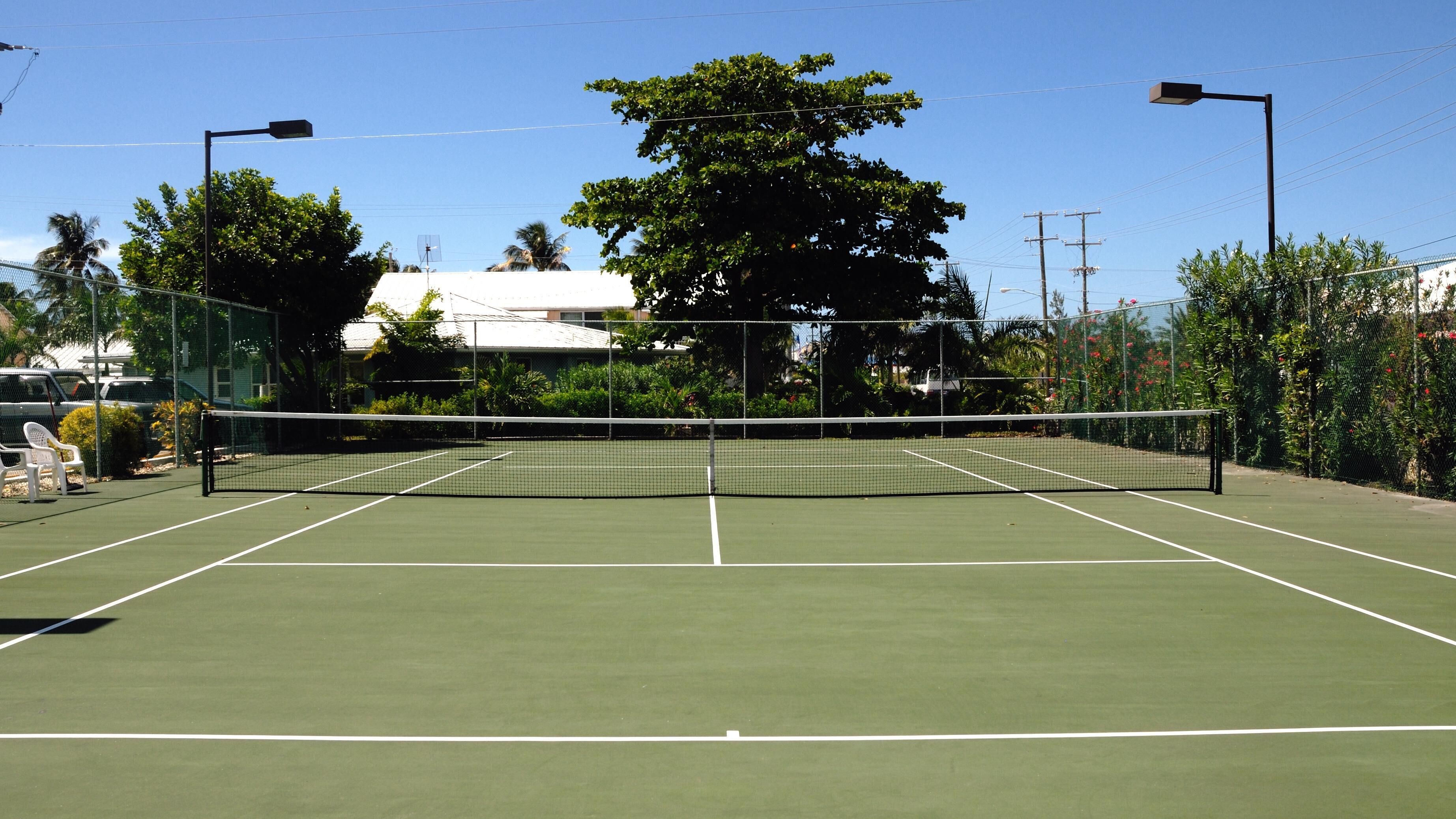 Una cancha de tenis con red, rodeada de follaje y árboles.