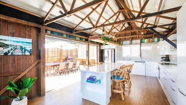 A spacious kitchen with wooden beams, a dining area with chairs, and a view of the outdoors. - Quarterdeck Wooli Australia (Wooli)