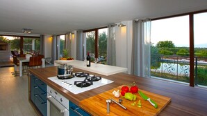 A modern kitchen with a large island, a dining area, and large windows with a view of greenery and a body of water.