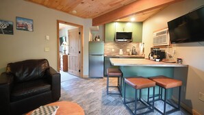 A modern kitchen with a built-in microwave, a large island with bar stools, and a flat-screen TV mounted above the island. - Renovated! Cute, 1 bdrm sleeps 2 Golf/ ski. pool and Wifi! new KING bed. (Mancelona)