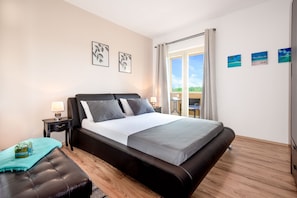 A bedroom with a large bed, a nightstand, a lamp, a window with curtains, and a view of the outdoors.