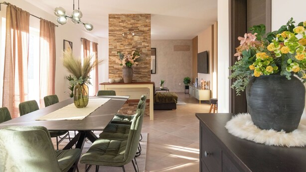 A modern dining area with a long table, green upholstered chairs, and a central island with a stone accent wall. - Villa Coridigo - High Position with Panorama View (Kringa)