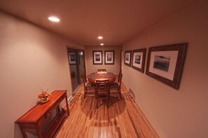A dining area with a wooden table and chairs, framed pictures on the walls, and a wooden console table with a vase of flowers.
