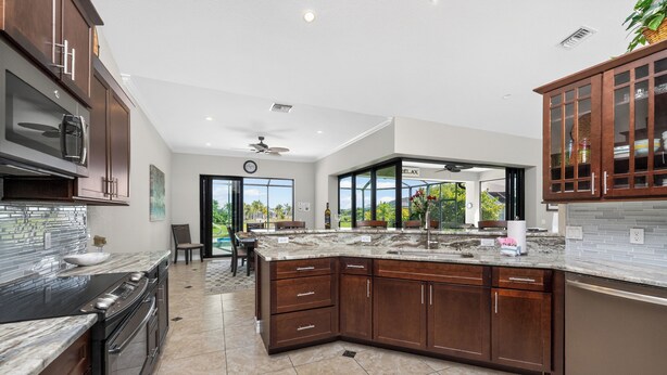 Una cocina moderna con armarios de madera oscura, una isla grande, electrodomésticos de acero inoxidable y vistas a través de la puerta de vidrio.