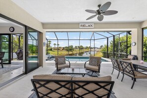 A poolside area with a ceiling fan, outdoor seating, and a view of a swimming pool and landscape.