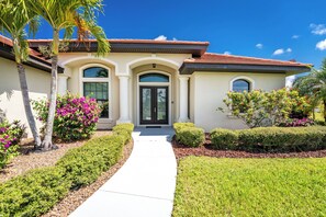 A two-story house with a front entrance, a covered porch, and a well-maintained garden with shrubs and flowering plants.