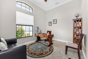 Un salon comprenant un canapé, un bureau, une chaise, une bibliothèque et une fenêtre donnant sur un jardin fleuri.
