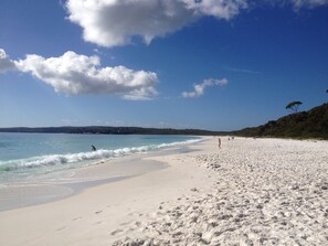 A beach with white sand, clear blue water, and a few people walking.