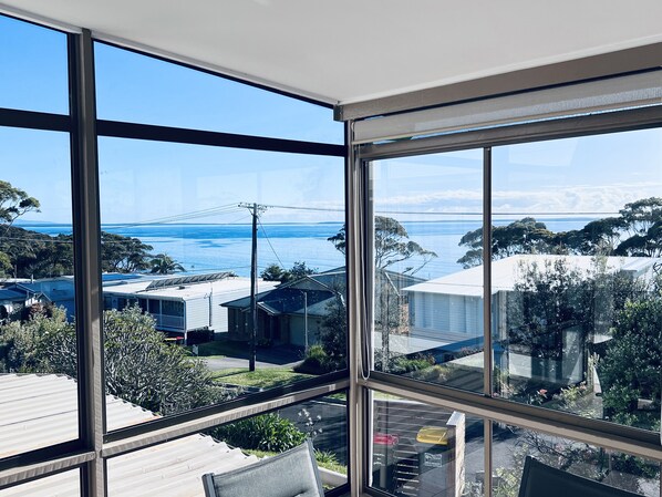 A room with large windows offering a view of the sea and surrounding buildings.