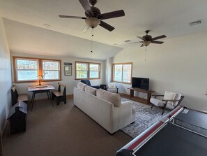 A spacious living room with a couch, a table, a TV, and two ceiling fans. - Perfect Lakefront Family Get-A-Way/ Private Dock/ Firepit / Sandy Beach (Center Ossipee)
