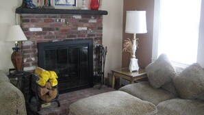 A living room with a brick fireplace, a sofa, a table with a lamp, and a window. - Beautiful Historic Home Centrally Located  (Provincetown)