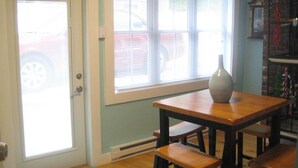 A room with a door, a window with blinds, a table with a vase, and a bookshelf. - Beautiful Historic Home Centrally Located  (Provincetown)