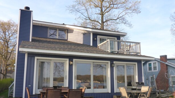 A two-story house with a deck, large windows, and outdoor furniture.